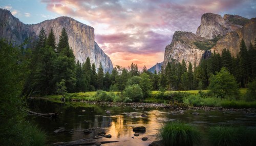 A serene landscape featuring towering cliffs, lush trees, and a reflective river under a colorful sunset sky.
