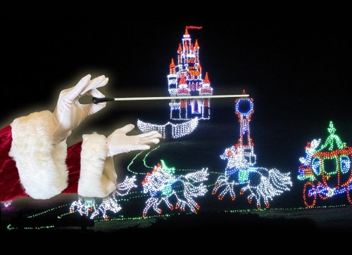 A gloved hand in a Santa suit gestures towards a colorful, illuminated holiday display featuring a castle and festive scenes.