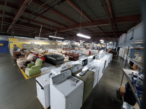 A spacious warehouse filled with various furniture items and appliances, including couches and washing machines.