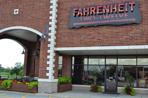 Exterior of Fahrenheit Two-Twelve restaurant, featuring a brick facade, large windows, and colorful flower planters.