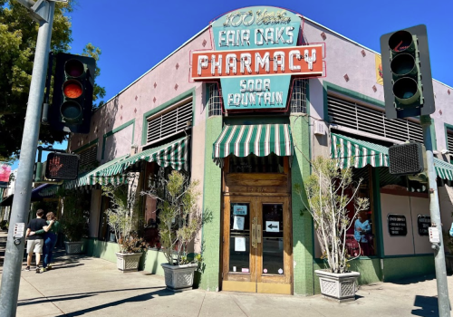 Historic pharmacy building with a soda fountain, featuring green accents and striped awnings, under a clear blue sky.