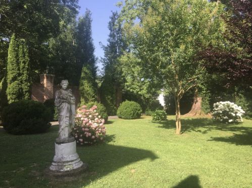 A serene garden scene featuring a statue, lush greenery, and blooming flowers under a clear blue sky.