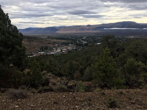 A panoramic view of a valley town surrounded by mountains and trees under a cloudy sky.