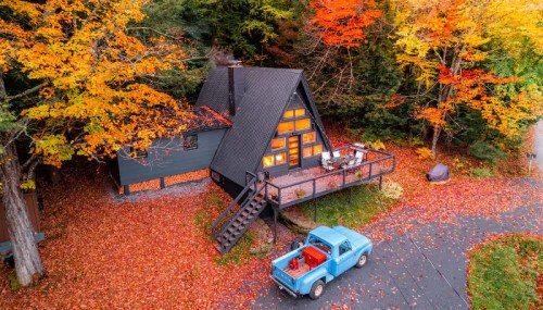 A cozy A-frame cabin surrounded by vibrant autumn foliage and a vintage blue truck parked nearby.