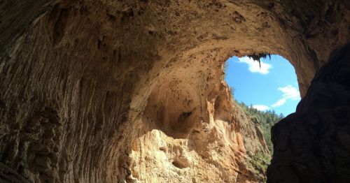 A large cave opening with rocky walls, revealing a blue sky and greenery in the background.