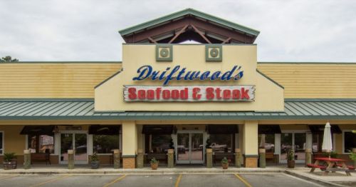 Exterior view of Driftwood's Seafood & Steak restaurant, featuring a colorful sign and outdoor seating area.
