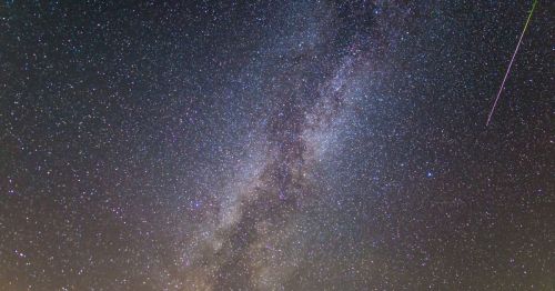 A stunning view of the Milky Way galaxy filled with stars, featuring a bright meteor streaking across the night sky.