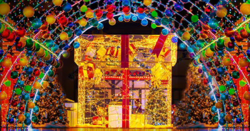 A vibrant holiday display featuring a large illuminated gift surrounded by colorful lights and decorated trees.