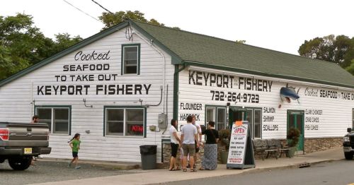 A seafood takeout shop named Keyport Fishery, featuring a white building with black signage and customers outside.