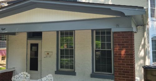 Front view of a house featuring a porch, two windows, and a brick accent wall.