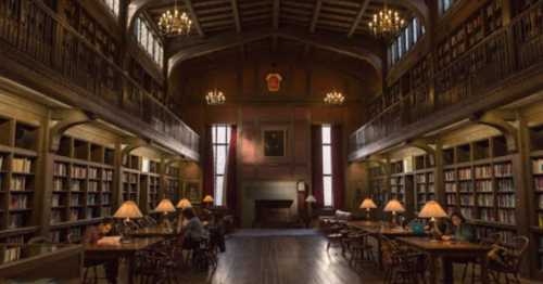 A grand library with high ceilings, wooden shelves, and chandeliers, featuring tables and people reading quietly.