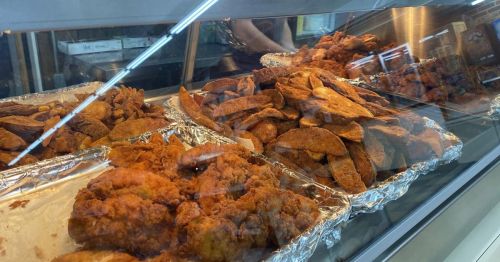 A display case filled with golden-brown fried chicken and crispy potato wedges on aluminum foil.