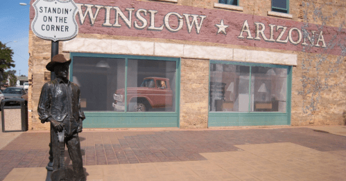 A bronze statue of a cowboy stands by a sign reading "Standin' on the Corner" in front of a historic building in Winslow, Arizona.