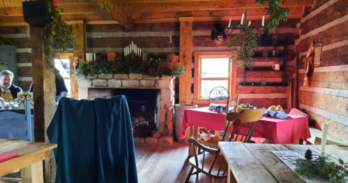 Cozy log cabin interior with a stone fireplace, festive decorations, and a dining table set for a gathering.