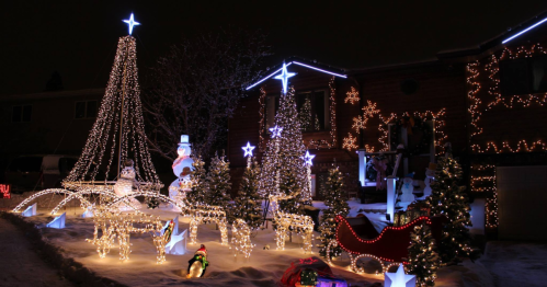 A festive display of Christmas lights featuring a tree, snowman, sleigh, and stars in a snowy yard at night.