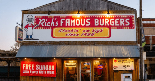 A vintage burger restaurant sign with "Rich's Famous Burgers" and a cartoon chef, featuring bright lights and a welcoming vibe.