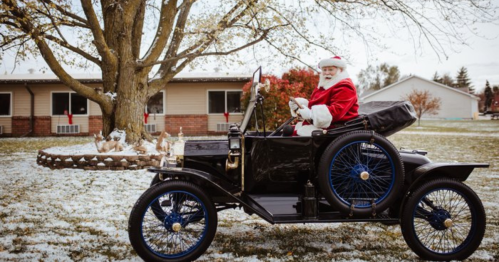 Santa Claus in a vintage car, waving, with a snowy landscape and geese in the background.