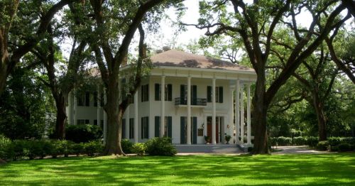 A large white house with columns, surrounded by lush green grass and tall trees.