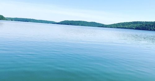 A serene lake surrounded by green hills under a clear blue sky, with gentle ripples on the water's surface.