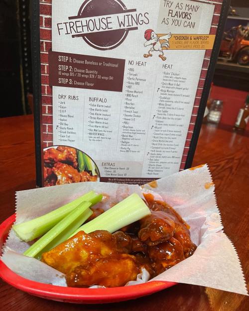 A basket of firehouse wings with celery sticks, next to a menu featuring various wing flavors and options.