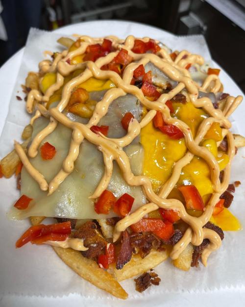 A plate of loaded nachos topped with melted cheese, diced red peppers, and a creamy sauce drizzled on top.