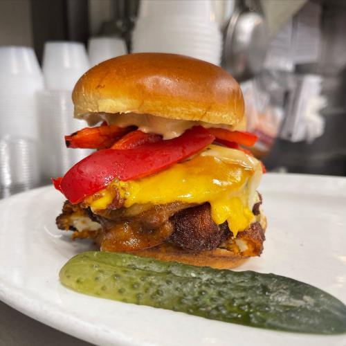 A juicy cheeseburger with lettuce, tomato, and pickles on a white plate, set against a blurred background.