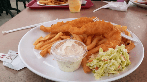 A plate of crispy fish fillets served with French fries, coleslaw, and a small cup of tartar sauce.