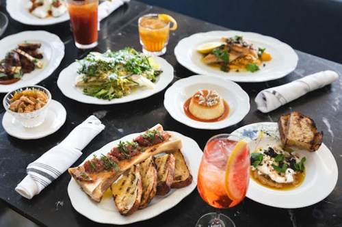 A table set with various gourmet dishes, including seafood, salads, and desserts, alongside colorful cocktails.