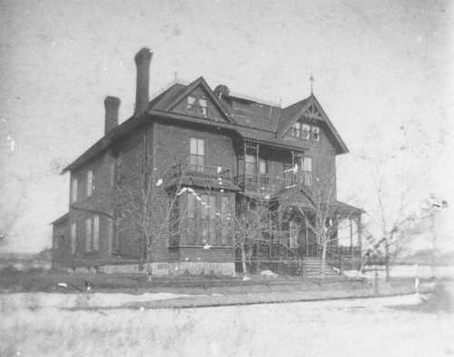 A historic two-story wooden house with a porch, surrounded by bare trees and a clear sky.