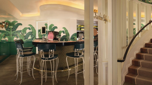 A stylish bar area with green tropical wallpaper, high stools, and a staircase leading to another level.