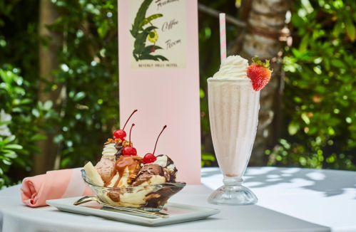 A delicious ice cream sundae with cherries and a milkshake topped with whipped cream and a strawberry, set outdoors.