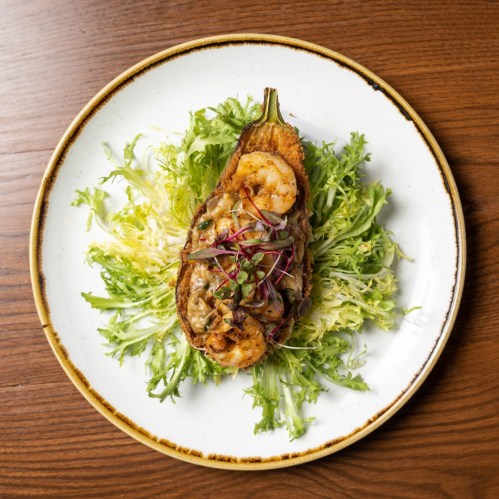 A beautifully plated dish featuring a stuffed eggplant topped with shrimp, served on a bed of fresh greens.