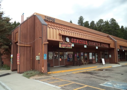 Exterior of Genesee County Store, a wooden building with a sloped roof, featuring a sign and outdoor seating area.