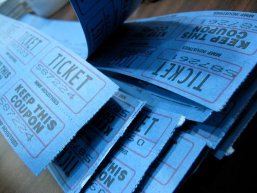 A stack of blue carnival tickets with red text, some partially rolled and showing the words "KEEP THIS COUPON."