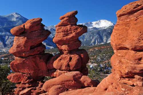 Red rock formations stand against a clear blue sky, with snow-capped mountains in the background.