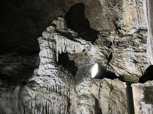 A spotlight illuminates unique rock formations in a dark cave, showcasing stalactites and stalagmites.