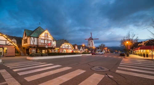 Charming street scene with European-style buildings, a windmill, and streetlights under a twilight sky.