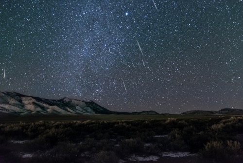 A starry night sky filled with shooting stars over a mountainous landscape and dark foreground.