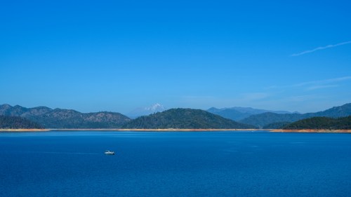 A serene lake surrounded by mountains under a clear blue sky, with a small boat on the water.