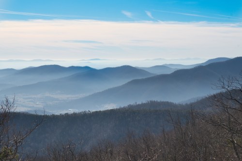 A panoramic view of misty blue mountains under a clear sky, with layers of hills fading into the distance.