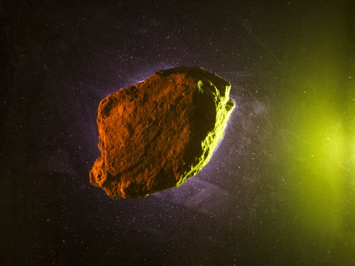A rocky asteroid floats in space, illuminated by green and orange light against a starry background.