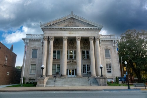 A grand, classical-style building with large columns and a staircase, set against a cloudy sky.