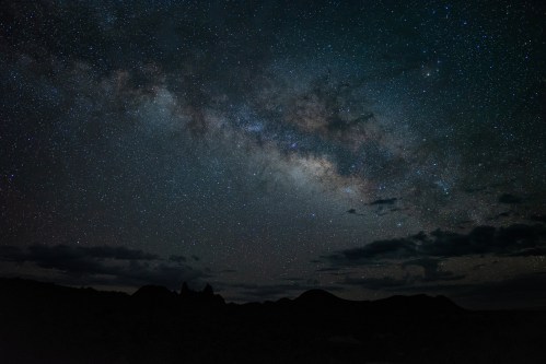 A starry night sky filled with the Milky Way, silhouetted mountains in the foreground against a dark backdrop.