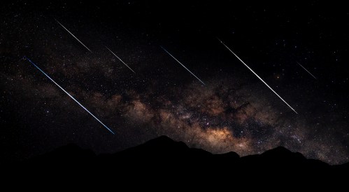 A starry night sky with a vibrant Milky Way and several shooting stars streaking across the darkness.