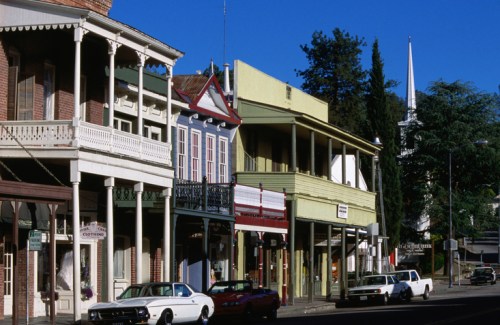 Historic buildings line a street, featuring colorful facades and parked cars under a clear blue sky.