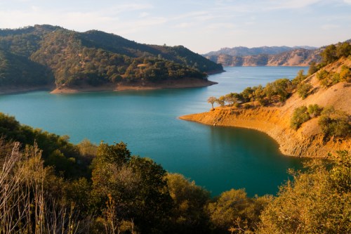 A serene lake surrounded by rolling hills and trees under a clear blue sky.