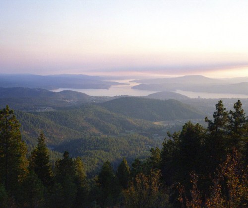 A serene landscape featuring rolling hills, a lake, and a soft sunset sky with hues of purple and orange.