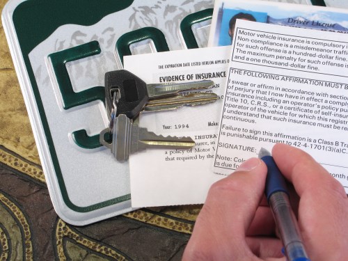 A close-up of car keys, a driver's license, and an insurance document on a textured surface.