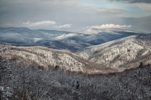 Snow-covered mountains stretch across the horizon under a cloudy sky, showcasing a serene winter landscape.