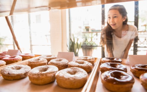 A girl gazes excitedly at a display of assorted donuts in a bakery.